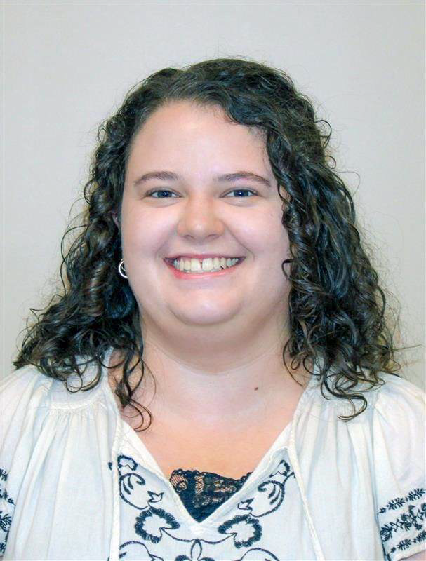 Ms. Kelsey Trimble, a Caucasian female with shoulder length brown curly hair, smiles at the camera wearing a white peasant top blouse with dark embroidery.