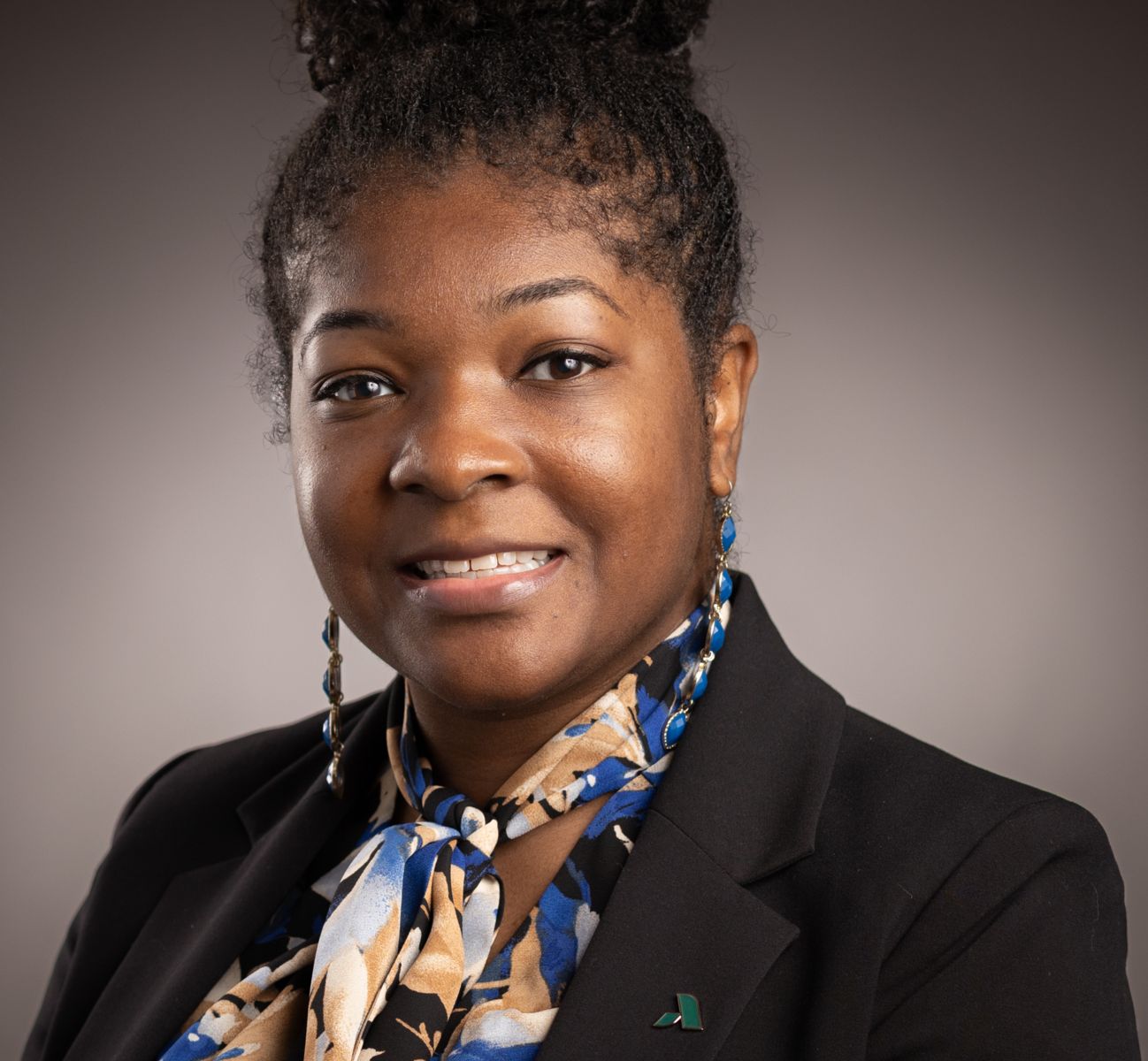 Dean Aherial Polite smiles at the camera wearing a colorful dress shirt and a black dress jacket with a green augusta tech pin.