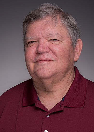 A Caucasian male with grey and black hair, Jim Poarch smiles at the camera and is wearing a maroon collared, button down dress shirt.