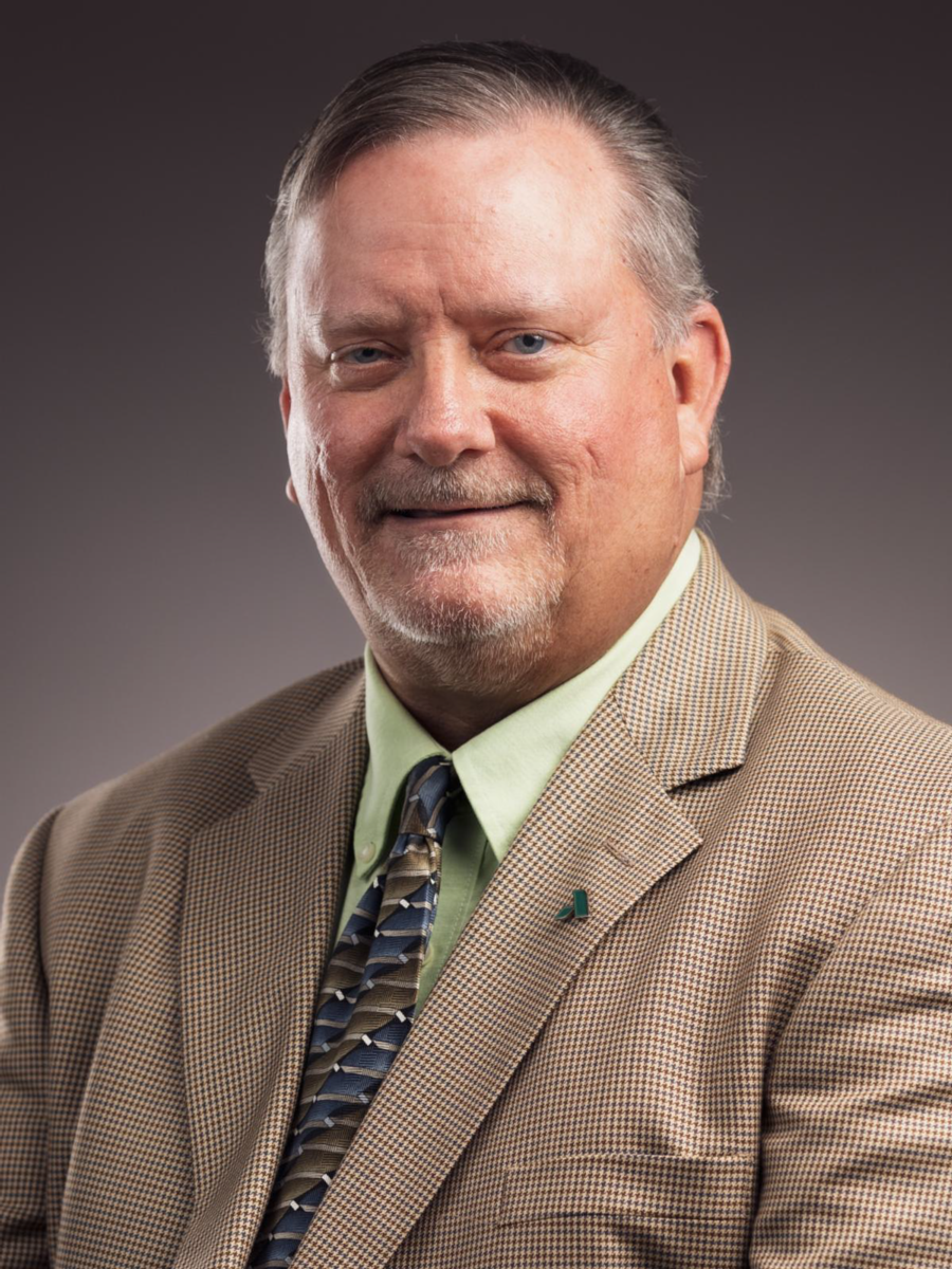 Mr. Jimmy Bostock, a Caucasian male, wears a brown and white patterned suit jack with a collared shirt and tie.
