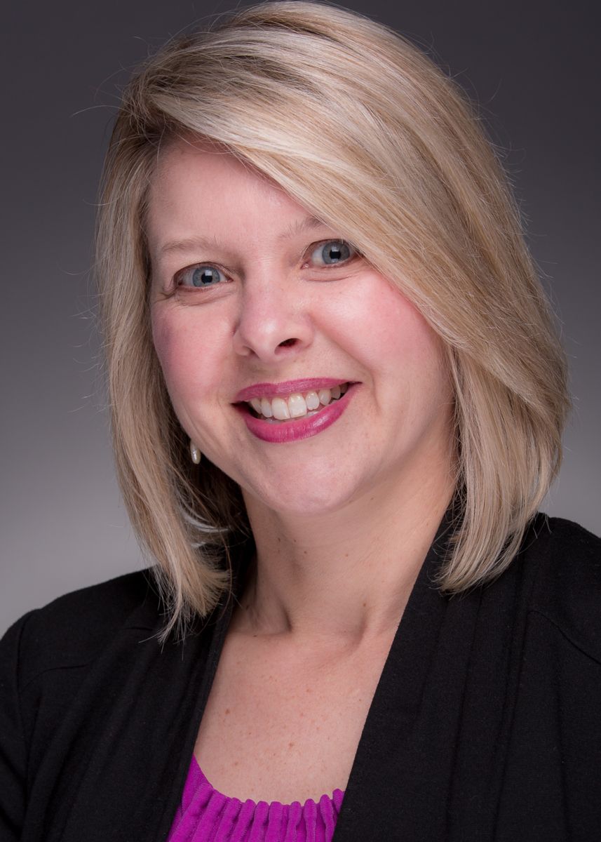 Mrs. Julie Langham, a Caucasian female with shoulder length blonde hair smiles wearing a fuschia sweater with a black dress jacket.